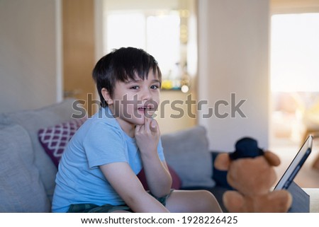 Portrait Active kid bitting his finger nails while looking at camera.Happy kid having fun watching cartoon or play game on tablet, Home schooling, Home learning or E-learning online education