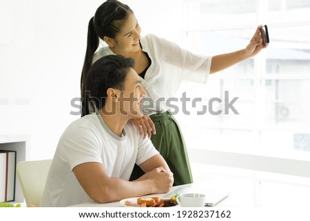 Young asian couple taking photo using smartphone during their breakfast at home. Beautiful woman making selfie with her boyfriend. Togetherness concept.