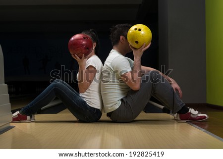 Young Couple Hiding Their Faces Behind Bowling Ball