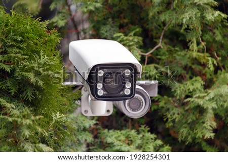 Covert video surveillance. CCTV security camera or radar for monitoring the speed of cars mounted among the trees. Video equipment for safety system area control outdoor, technology concept. Royalty-Free Stock Photo #1928254301