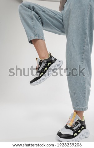 Fashion woman model with blue jeans in stylish sports shoes on a white background. Female legs with trendy running shoes.