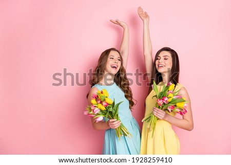 Photo of optimistic nice long hairdo ladies hold flowers arm up wear pastel dress isolated on pink color background