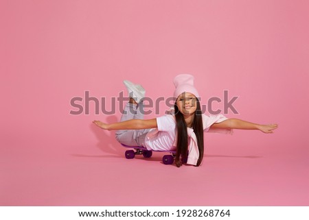 smiling little child girl riding on skateboard over pink background. kid having fun