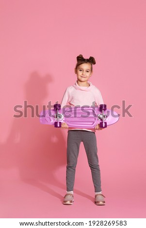 little child girl with pink skateboard in casual clothes on pink background.