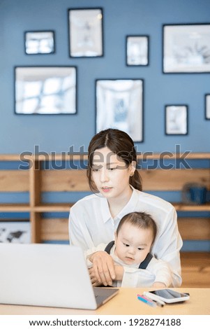 A woman holding a baby and operating a laptop