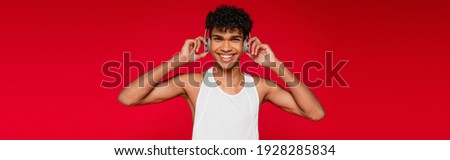 happy african american man adjusting wireless headphones isolated on red, banner