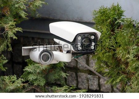 Covert video surveillance. CCTV security camera or radar for monitoring the speed of cars mounted among the trees. Video equipment for safety system area control outdoor, technology concept. Royalty-Free Stock Photo #1928291831