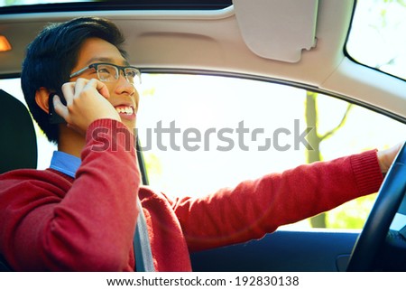 Young asian man driving car and speaking on mobile phone