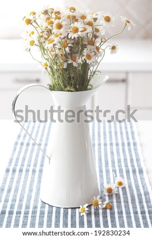 Bouquet of simple chamomiles in vintage pitcher on kitchen table