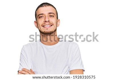 Hispanic young man wearing casual white t shirt happy face smiling with crossed arms looking at the camera. positive person. 