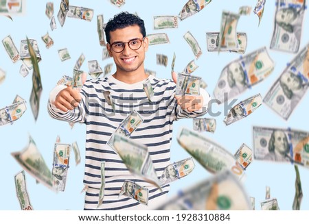 Hispanic handsome young man wearing casual clothes and glasses approving doing positive gesture with hand, thumbs up smiling and happy for success. winner gesture.