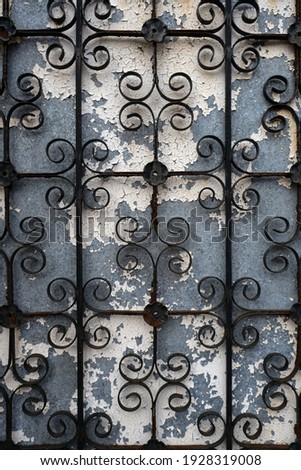 Wrought iron fence or gate on a weathered blue wall with cracked white paint.