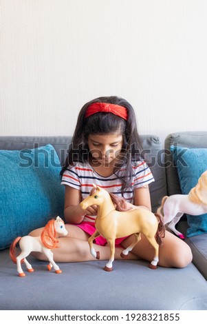 Little girl playing playing with her toy horses on the sofa