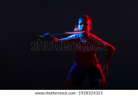 Kid playing badminton isolated on black background in mixed light. Blue and red filter. Sports background for product display, banner, or mockup
