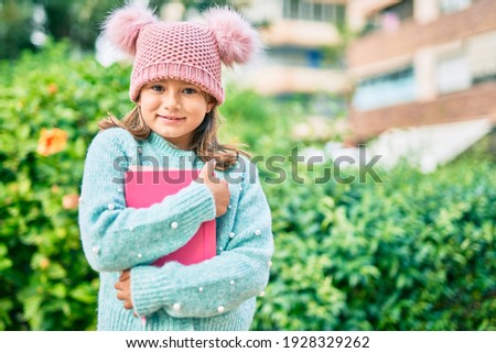 Adorable student child girl smiling happy holding book at the park.
