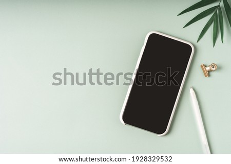 Flat lay of mobile smart phone with blank screen of gadget. Digital cell phone with copy space area on green background with pencil and leaf