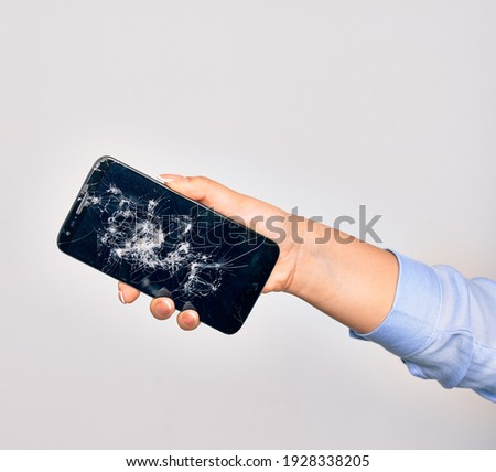 Hand of caucasian young woman holding broken smartphone showing craked screen over isolated white background