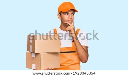 Young handsome african american man holding delivery package serious face thinking about question with hand on chin, thoughtful about confusing idea 