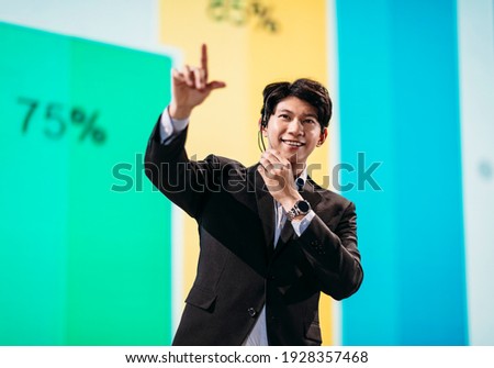 Male Asian Speaker Stands on Stage for Business Presentation  Royalty-Free Stock Photo #1928357468