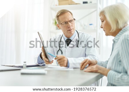 Serious male doctor having appointment with old woman in clinic