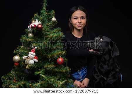 Portrait of a Labrador Retriever dog with its owner, near the new year's green tree. The picture was taken in a photo Studio on a black background.