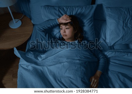 people, bedtime and rest concept - sleepless asian woman lying in bed at night Royalty-Free Stock Photo #1928384771