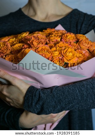A girl in a dark sweatshirt hugs a beautiful bouquet of roses wrapped in decorative paper with both hands. No recognizable people on vertical photo	