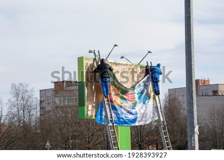 Workers hang an advertising banner at a height from the ladders
