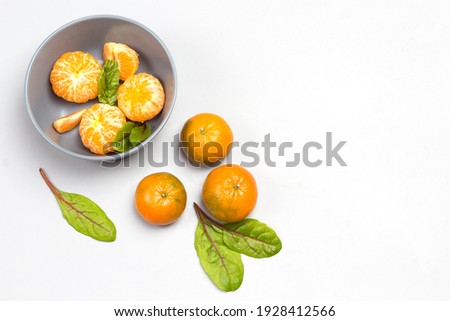 Peeled tangerines and chard leaves in gray bowl. Whole tangerines and chard leaves on table. Grey background. Top view. Copy space
