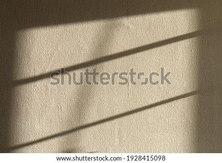 Rectangular spot of light with diagonal stripes of shadow on abstract textured light beige wall surface. Rough wall with lighted and shaded areas and with gradient of light-shadow of vertical borders
