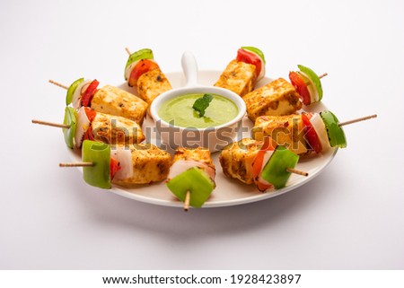 Starter snack Paneer Tikka with stick in plate with green chutney isolated over white background. Indian cuisine dish with grilled cottage cheese with vegetables and spices Royalty-Free Stock Photo #1928423897