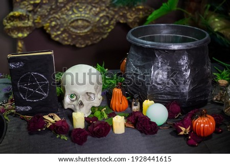 Black book with pentagram, skull and cauldron on the table with witchcraft ingredients. Halloween witch altar concept.