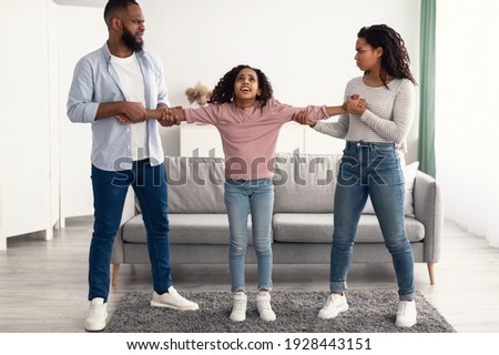 Divorce Concept. Portrait of angry African American parents fighting over their child, mad man and woman quarrelling, pulling daughter's hands in different directions. Domestic Violence, Separation Royalty-Free Stock Photo #1928443151