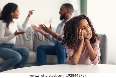 Divorce And Domestic Violence. Portrait of upset African American daughter looking through the window while her angry parents fighting in the background, depressed child feeling lonely Royalty-Free Stock Photo #1928443757