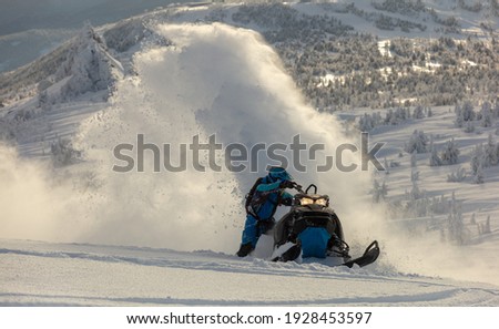 a guy on a mountain snowmobile skids and pushes full throttle, letting out large fountains of snow from under the tracks. bright skidoo motorbike and suit without brands. Winter fun. panoramic view