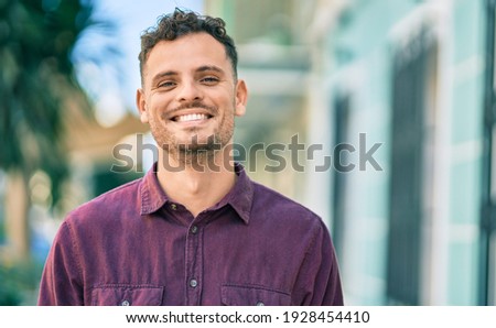 Young hispanic man smiling happy standing at the city. Royalty-Free Stock Photo #1928454410