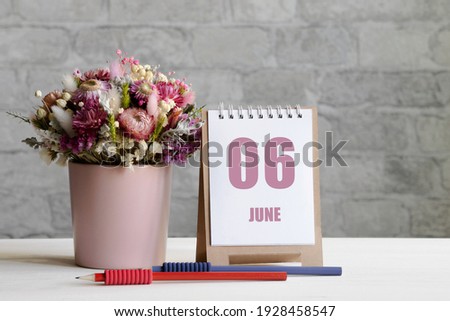 june 06. 06th day of the month, calendar date.A delicate bouquet of flowers in a pink vase, two pencils and a calendar with a date for the day on a wooden surface..