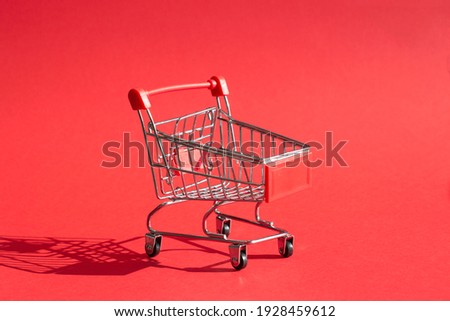 Small miniature supermarket trolley on dark red background, close up with empty space