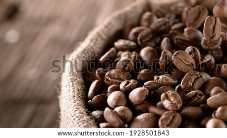 Falling Roasted Coffee Beans into Jute Bag, close-up. Royalty-Free Stock Photo #1928501843