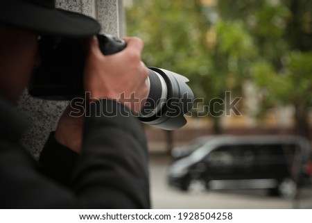 Private detective with modern camera spying on city street, closeup