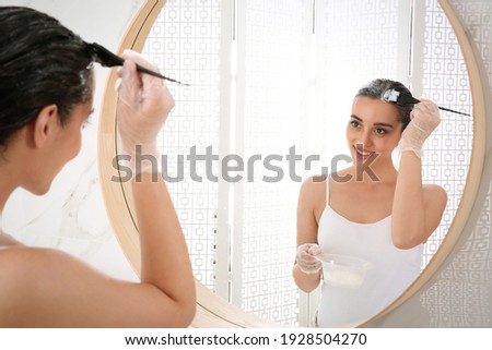 Young woman applying dye on hairs near mirror indoors Royalty-Free Stock Photo #1928504270