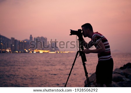 Silhouette of photographer with tripod. Young man photographing urban skyline. Hong Kong at dusk. 