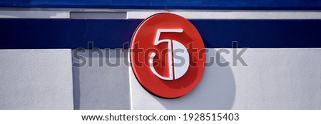 Building has a red circle displaying the number five.  Stripe runs length of building and is white.