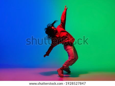 Inspiration. Stylish sportive girl dancing hip-hop in stylish clothes on colorful background at dance hall in neon light. Youth culture, movement, style and fashion, action. Fashionable bright Royalty-Free Stock Photo #1928527847