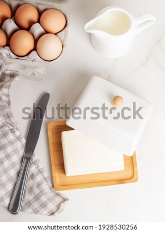Block of butter in butter dish with milk and eggs on a marble background. 