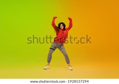 Dynamic. Stylish sportive girl dancing hip-hop in stylish clothes on colorful background at dance hall in neon light. Youth culture, movement, style and fashion, action. Fashionable bright portrait.
