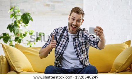 excited man taking selfie on mobile phone while showing thumb up