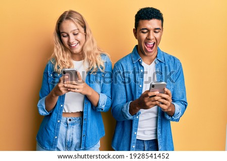 Young interracial couple using smartphone smiling and laughing hard out loud because funny crazy joke.  Royalty-Free Stock Photo #1928541452