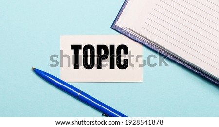 Notepad, white pen and card with the inscription TOPIC on a blue background. View from above