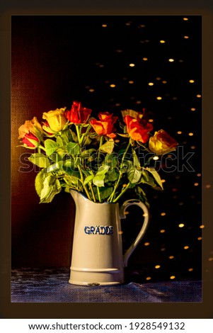 Bouquet of roses in an old cream jug against a dark background with texture and points of light. The inscription on the jug means cream